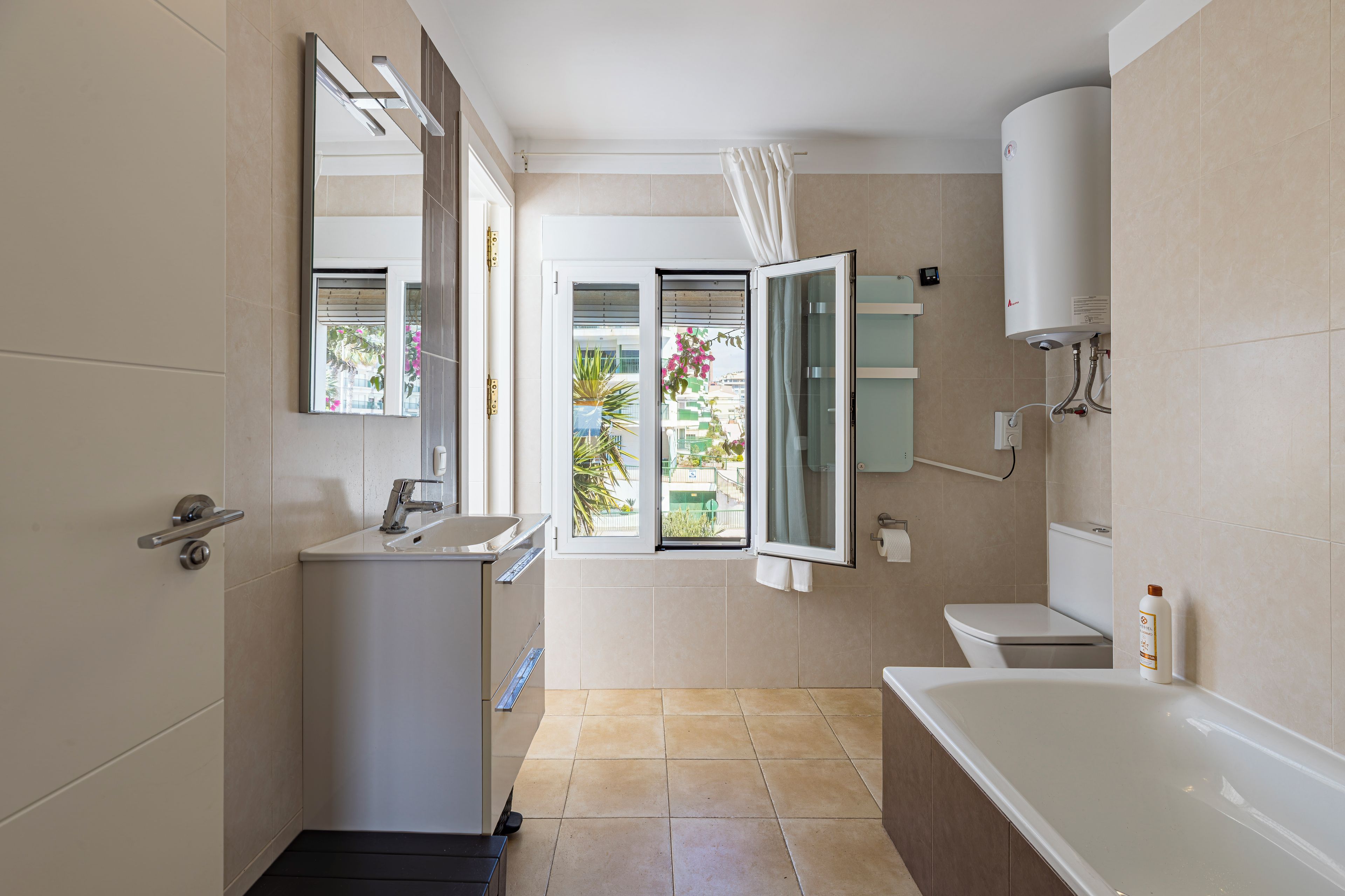Une salle de bain moderne équipée d’une baignoire, de toilettes, d’un lavabo et d’une fenêtre donnant sur l’extérieur.