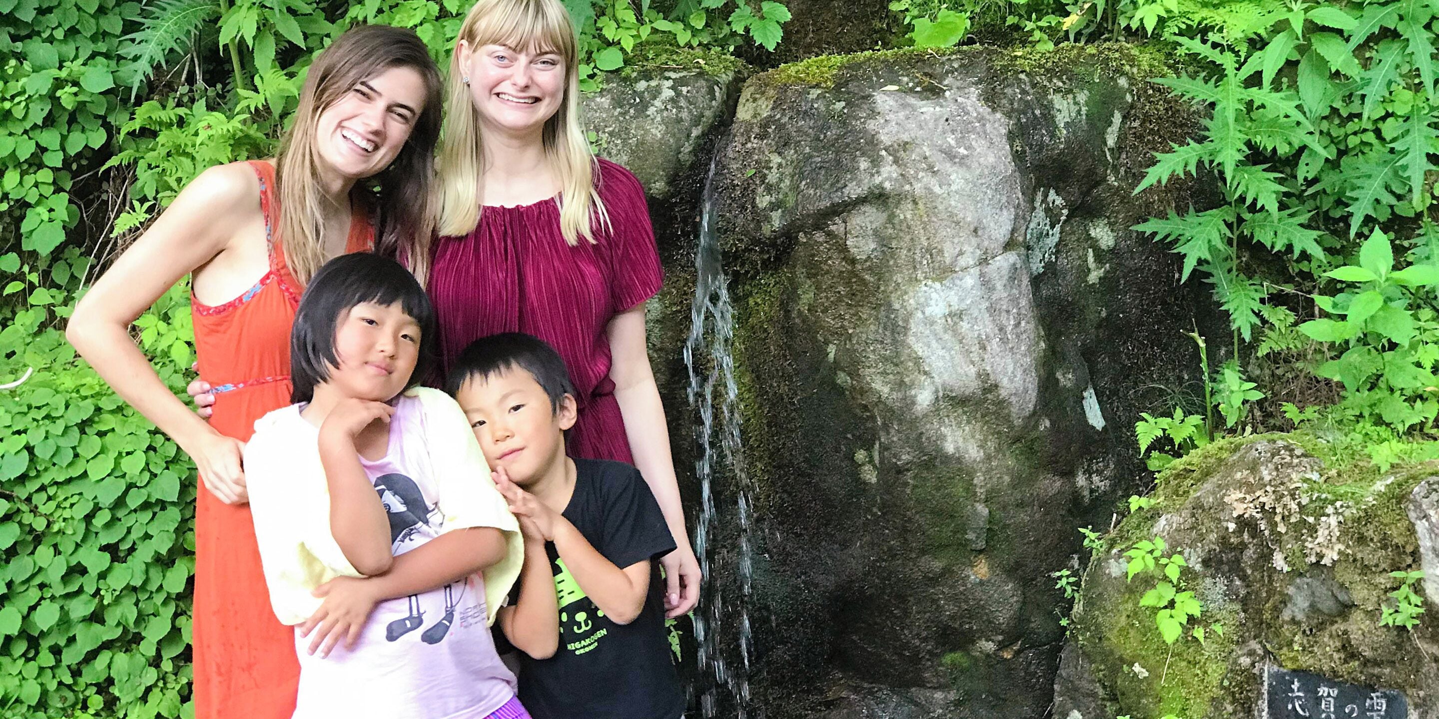 Una familia de cuatro personas posando frente a una roca cubierta de musgo y una pequeña cascada.
