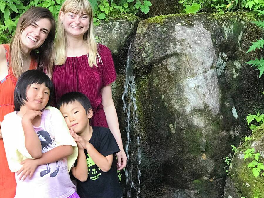 A family of four posing in front of a moss-covered rock with a small waterfall.