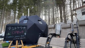 An outdoor sauna tent with a sign indicating it is open, surrounded by trees and camping equipment. - Sachinoyu Hotel Shiga Kogen (Yamanouchi)