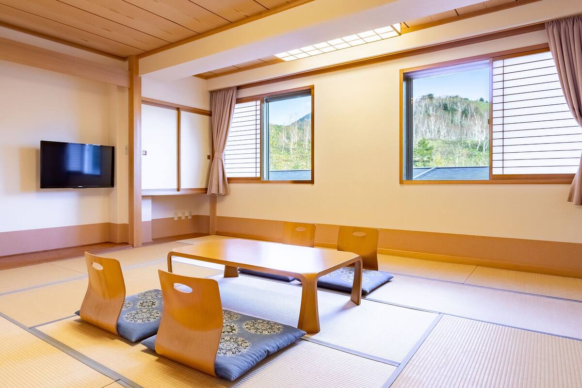 Tatami-mattoilla päällystetty huone, jossa on matala pöytä ja tyynyjä, televisio ja liukuvat ovet.