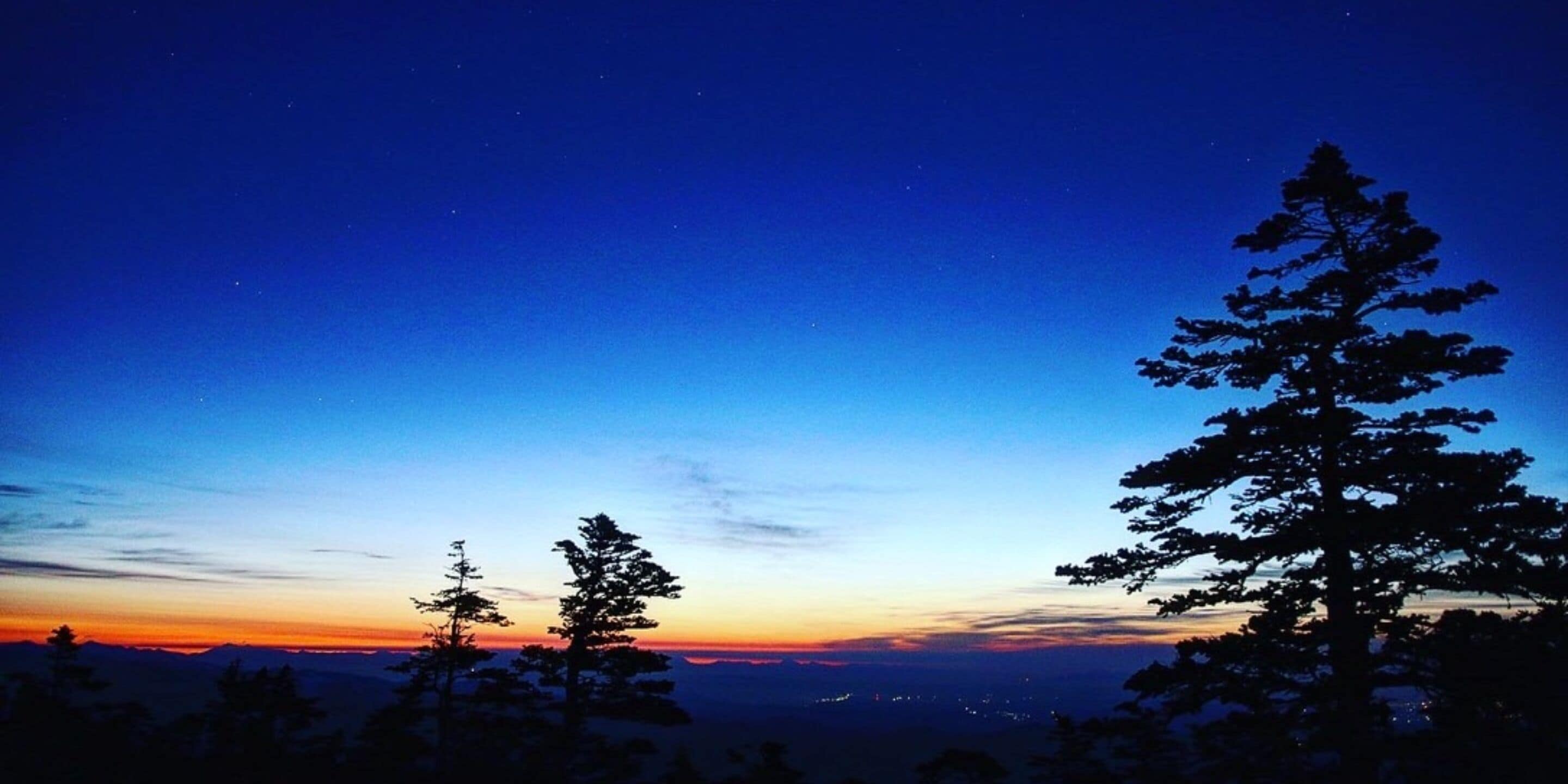 A night sky with stars and a silhouette of a mountain range.