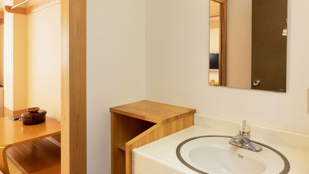 Une chambre d’hôtel avec une table de chevet en bois, un lavabo blanc avec un miroir et une armoire en bois.