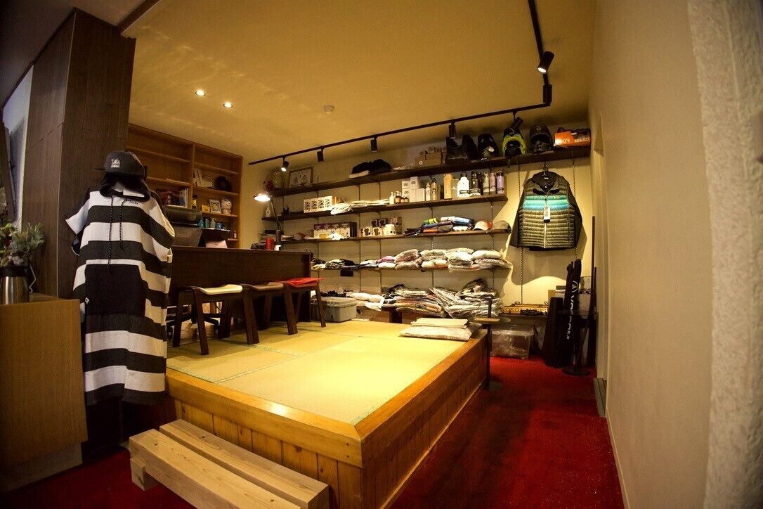 Een kamer met een houten platform, planken met opgevouwen kleding en een etalagepop in een gestreept shirt.