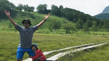 A person standing in a grassy field with a hilly landscape in the background.