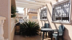 A covered outdoor patio with a table and chairs, a potted plant, and a window with a metal grill. - Excellent value villa with communal pool, 5minute beach & golf  (Los Alcazares, San Javier)
