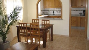 A dining area with a wooden table and chairs, a potted plant, and a kitchen with wooden cabinets and a tiled backsplash. - Excellent value villa with communal pool, 5minute beach & golf  (Los Alcazares, San Javier)