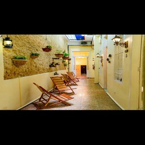Un couloir avec des chaises en bois, des jardinières suspendues et des lampes fixées au mur.