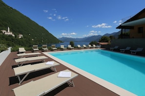 A swimming pool with lounge chairs, a wooden deck, and a mountainous backdrop.