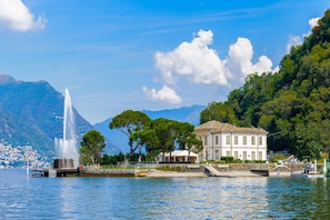 A waterfront property with a fountain, a large white building, and a mountainous backdrop.