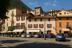 A street view with parked cars, a restaurant named 'RISTORANTE BARCHETTA,' and buildings with balconies.