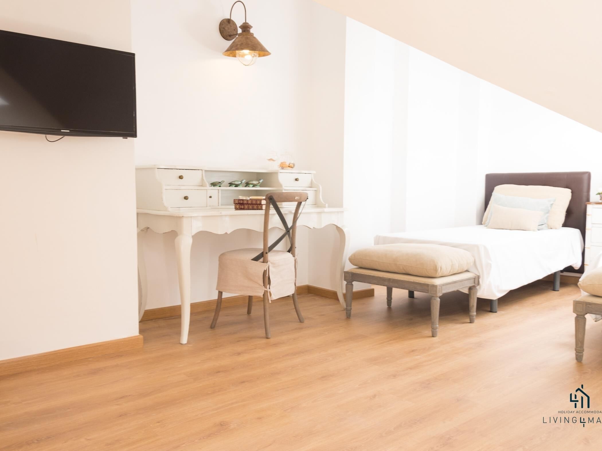 Un dormitorio con cama, escritorio, silla y televisor montado en la pared.