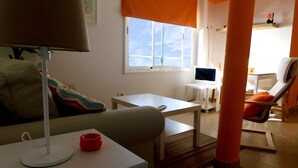 Ein Wohnzimmer mit einer Couch, einem Couchtisch, einem Fernseher und einem Schreibtisch mit einem Computer.