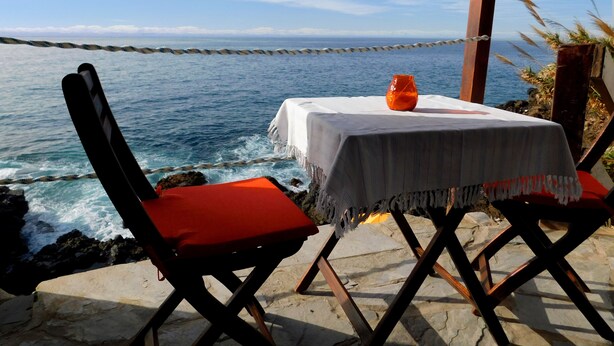 Ein Tisch mit weißem Tischlein und einer Vase, auf einer Steinterrasse mit Blick aufs Meer.