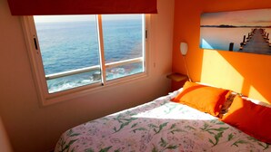 Ein Schlafzimmer mit Bett, einem Fenster mit Meerblick und einem Gemälde an der Wand.
