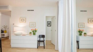 A modern, minimalist room with a white dresser, a black chair, and a small table with a vase of flowers.