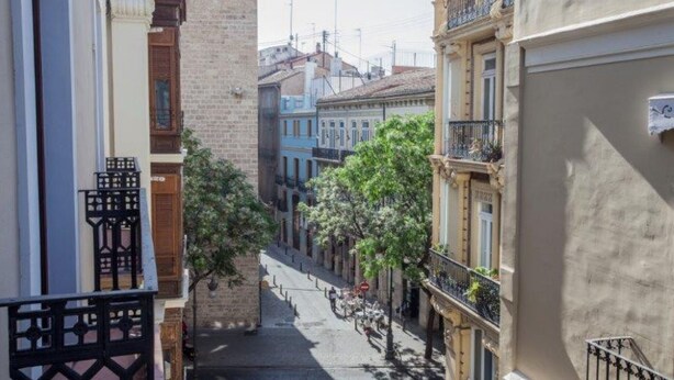 A narrow street with buildings on either side, featuring balconies and a clear sky.