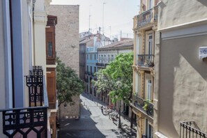 A narrow street with buildings on either side, featuring balconies and a clear sky.
