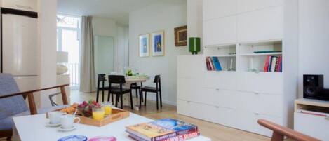 Un salon moderne avec un coin repas, une bibliothèque et une cuisine visible au fond.