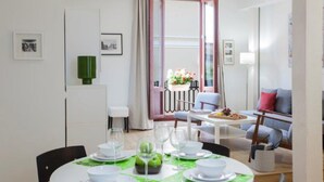 A modern dining area with a round table set for four, a sofa, and a view of a balcony with flowers.