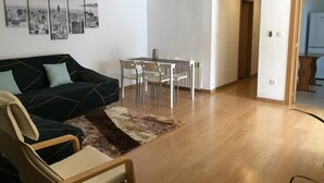 A modern living room with a sofa, a dining table with chairs, and a cityscape artwork on the wall.