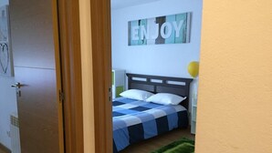 A bedroom with a bed, a green rug, and a wall sign that says "ENJOY".