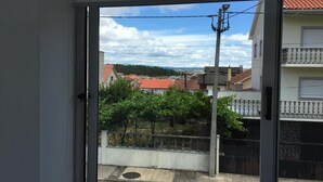 A view from a window with a metal gate and a paved area in the foreground, and buildings with red roofs in the background.