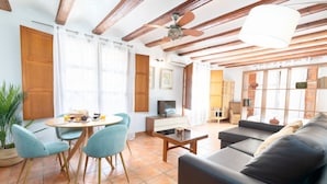 A living room with a sofa, a dining table with chairs, a television, and a ceiling fan.
