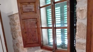 Ein rustikaler Essbereich mit Holztisch und -stühlen, einer Steinwand und einem Fenster mit Fensterläden.