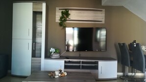 A modern living room with a flat-screen TV mounted on the wall, a white entertainment unit, and a dining area with a table and chairs. - EL Valle Dúplex, Puerto Rico (puerto rico)