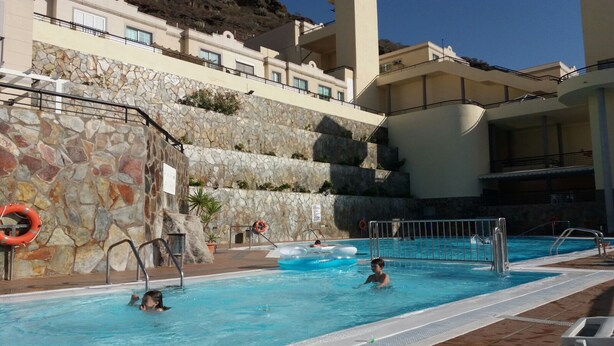 A swimming pool with a stone wall and a lifebuoy, surrounded by a building with balconies. - EL Valle Dúplex, Puerto Rico (puerto rico)