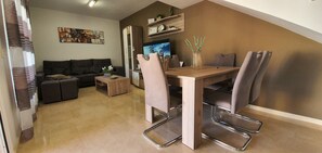 A modern living room with a sofa, a coffee table, a dining table with chairs, a TV, and a decorative vase.