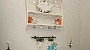 En liten matplats med ett vitt bord och stolar, en hylla ovanför med tallrikar och en modell av ett skepp, och en växt på väggen.