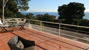 Eine Terrasse mit Korbmöbeln, Meerblick und einem weißen Geländer.