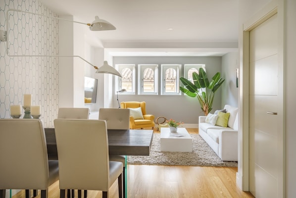 A modern living room with a dining area, a yellow armchair, a white sofa, and a large plant.
