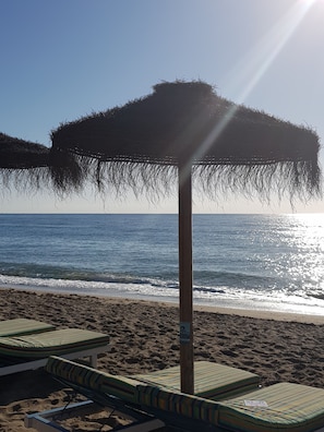 A beach with lounge chairs and a thatched umbrella. - Luxury villa, sea views, private garden, peaceful, communal pool, close to sea (La Cala de Mijas)