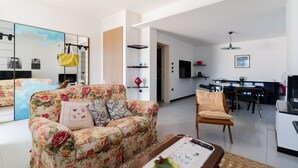 A living room with a floral sofa, a wooden chair, a coffee table, and a dining area with a table and chairs. - Entrance, living room, kitchen, 3 spacious rooms, 4p bedroom, 2 bathrooms, garden, place car (Tuglie)