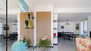 A modern living room with a dining area, featuring a sofa, a coffee table, and a dining table with chairs. There is a potted plant and a wall-mounted shelf with decorative items. - Entrance, living room, kitchen, 3 spacious rooms, 4p bedroom, 2 bathrooms, garden, place car (Tuglie)