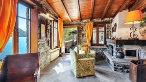 A cozy room with stone walls, wooden beams, a fireplace, and a view of a lake.