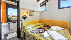 A hotel room with a bed, a window with a view of a clock tower, a bathroom with a sink and towel rack, and a magazine on the bed.