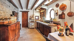 A rustic kitchen with wooden cabinets, a stone wall, and a variety of kitchen utensils and cookware displayed on the wall.