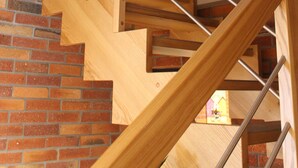 A wooden staircase with metal railings, leading to a brick wall and a window with a stained glass design.