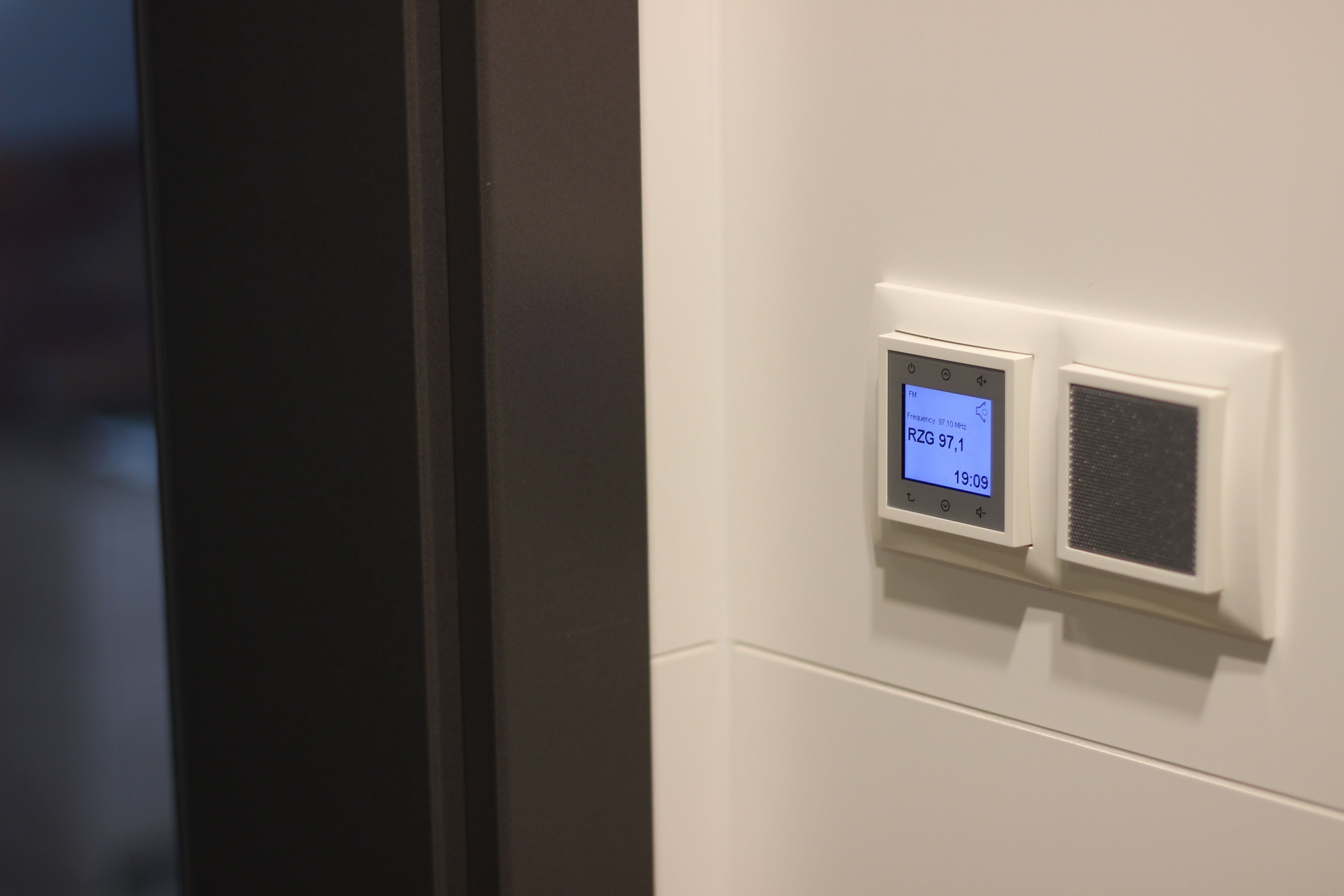 Ein Thermostat mit digitaler Anzeige an einer weißen Wand.