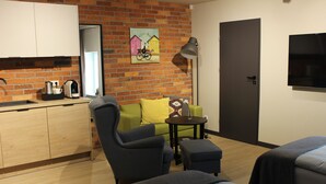 A modern hotel room with a brick wall, a sofa, a dining table, a TV, and a bed.