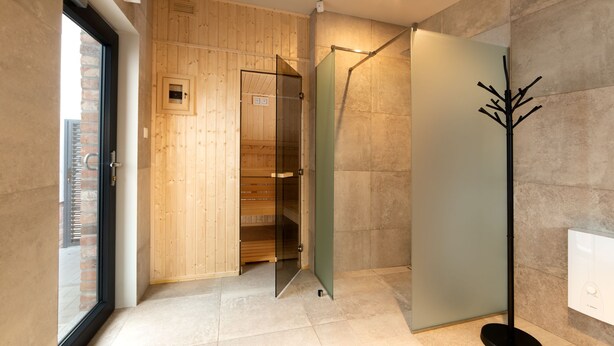 A modern bathroom with a wooden panel wall, a glass shower enclosure, and a black floor lamp.