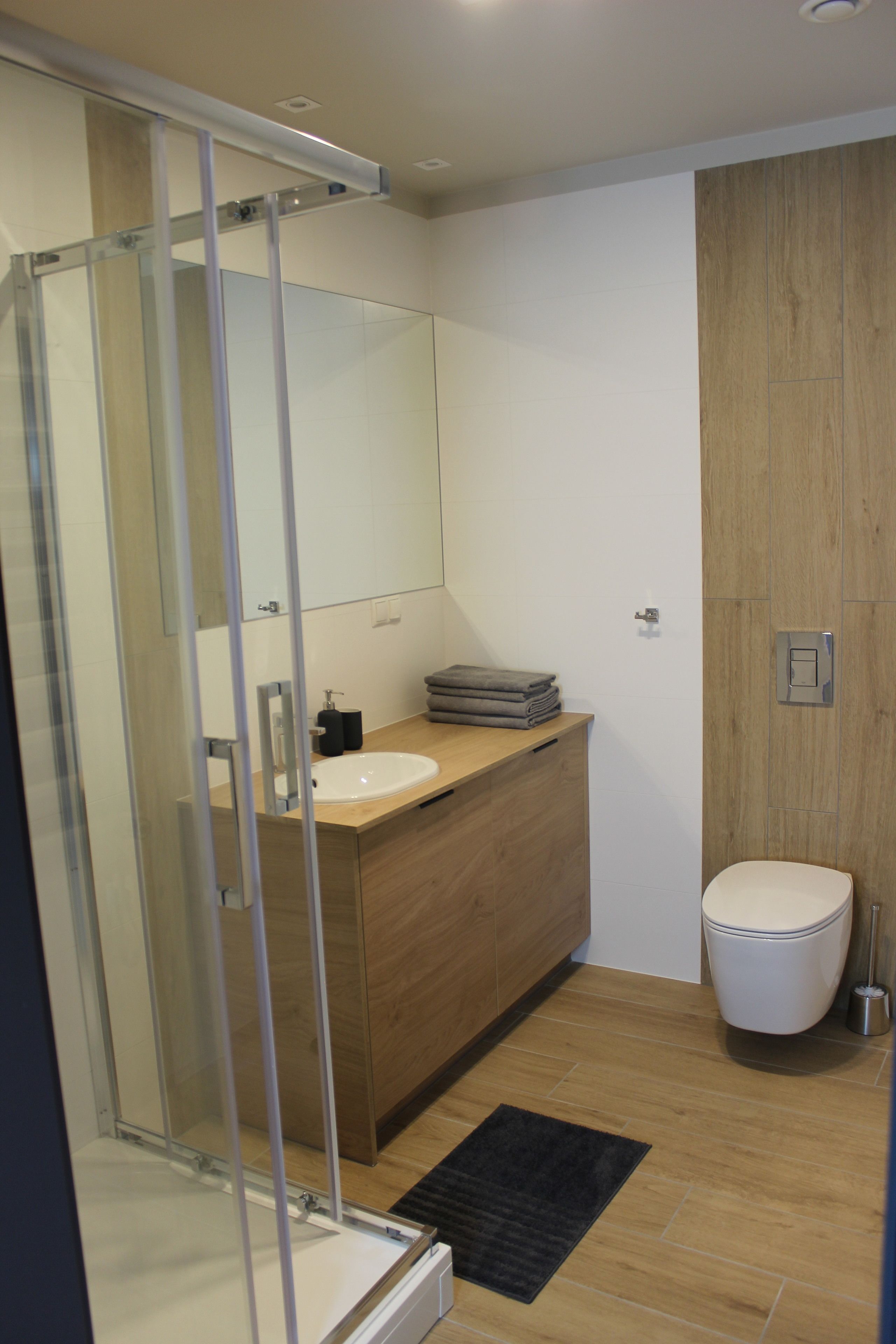 Ein modernes Badezimmer mit Duschkabine aus Glas, einem Holzwaschtisch, einem weißen Waschbecken und einer Toilette.