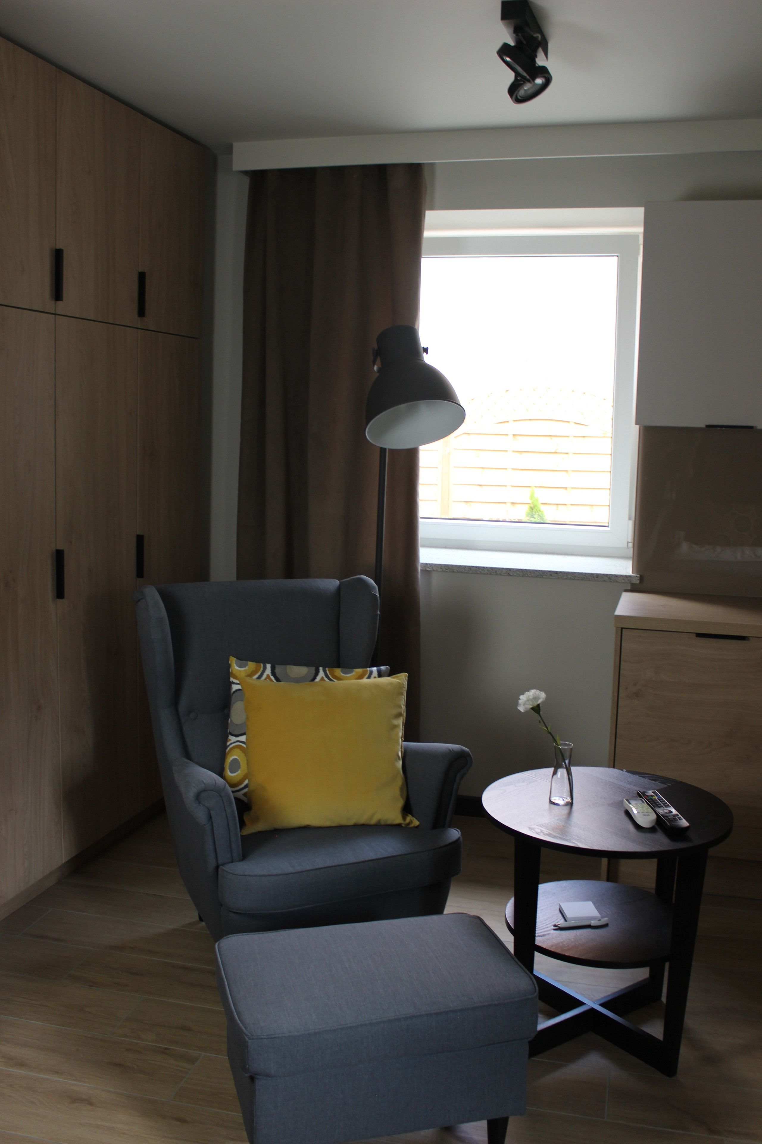 A modern room with a grey armchair, a small round table with a vase of flowers, and a wooden wardrobe.