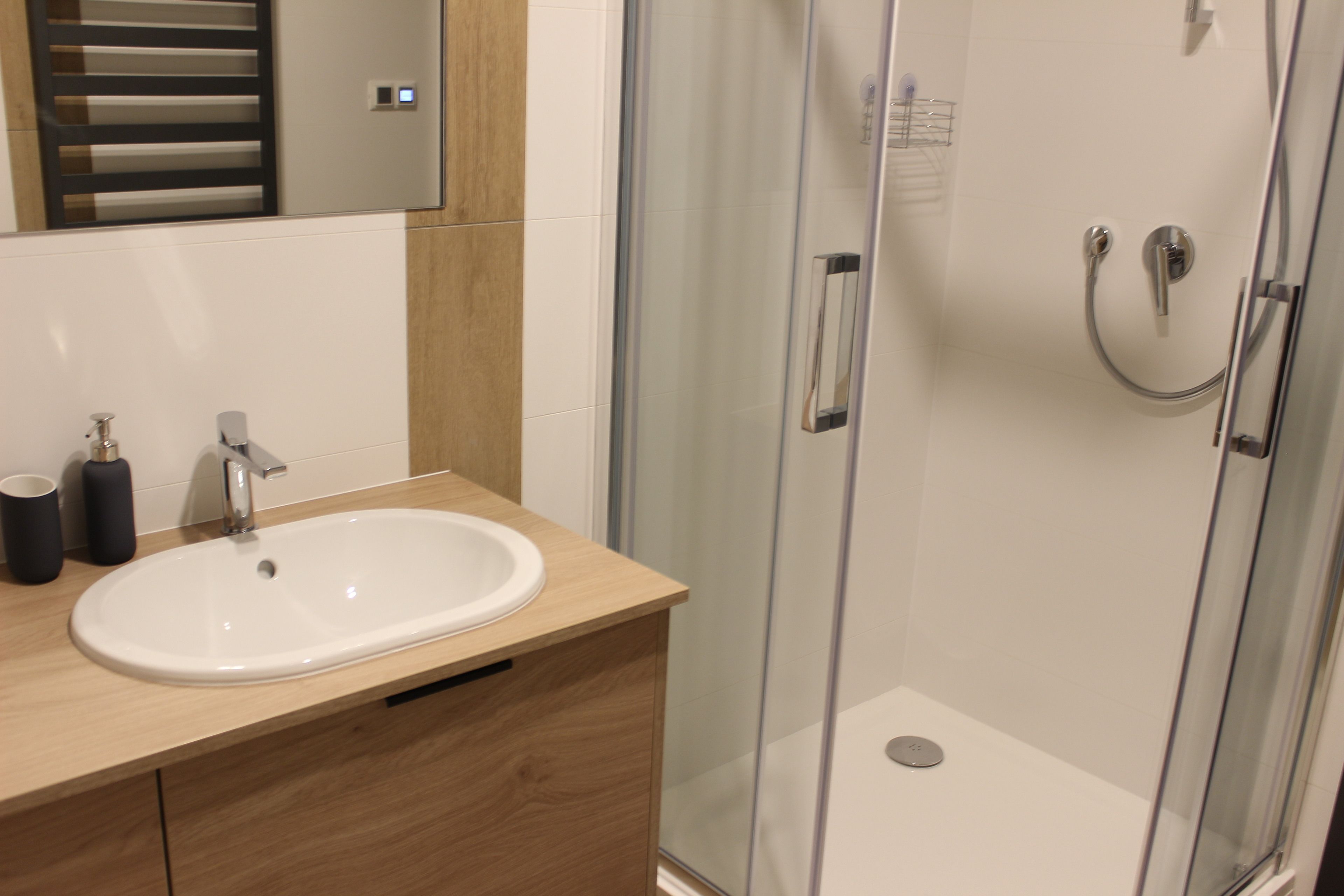 A modern bathroom with a glass-enclosed shower, a white sink, and wooden cabinetry.