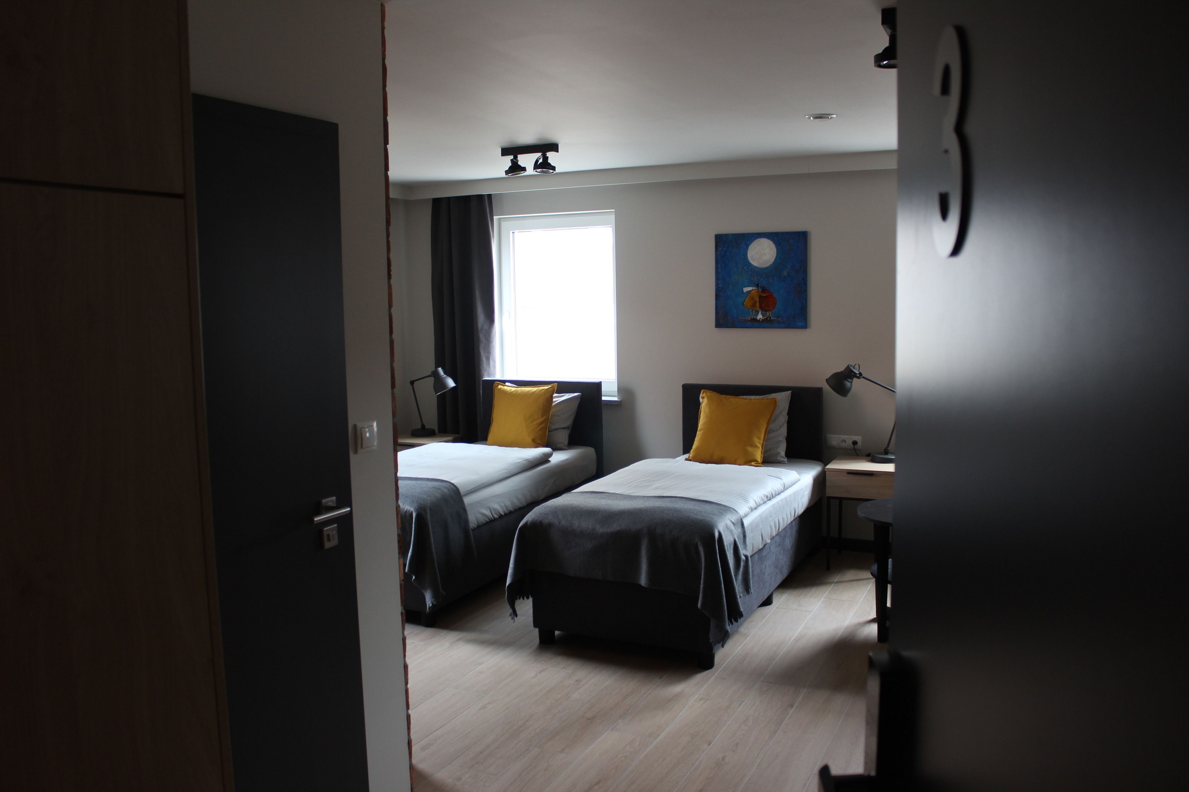 A room with two beds, a desk, a lamp, and a painting on the wall.