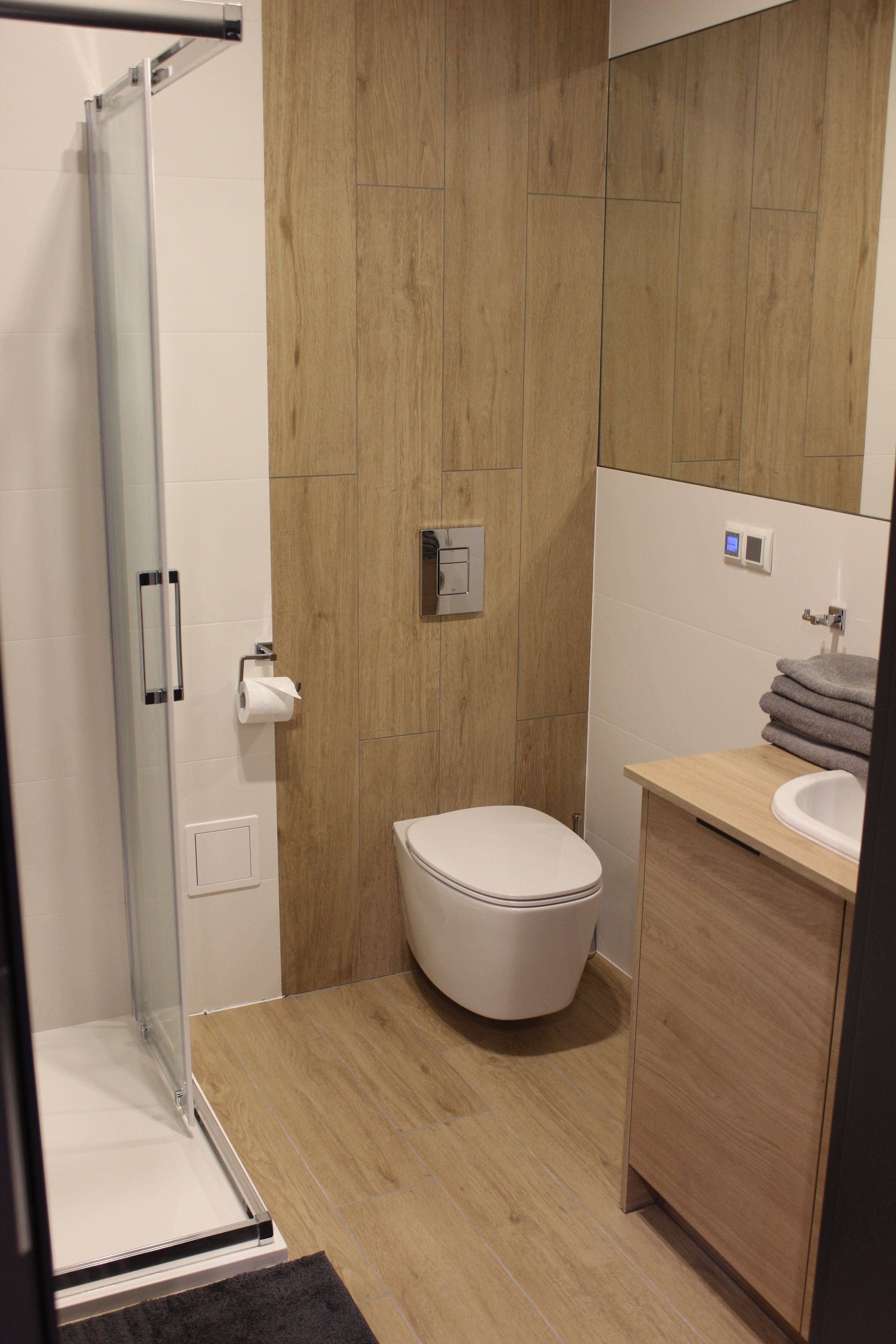 A modern bathroom with a glass shower enclosure, a toilet, and a wooden vanity with a sink.